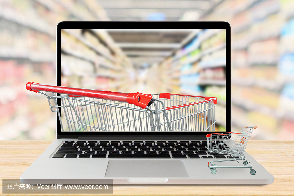 超市过道模糊的背景与笔记本电脑和购物车木桌子上的网上杂货概念